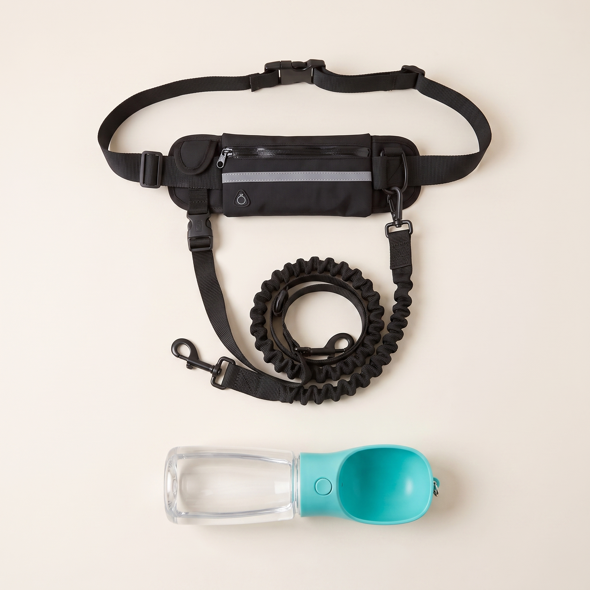 The Walk Kit laid out flat: the black WANDRA Roam Lead hands-free waist belt with its zipped pouch and coiled bungee lead above, and the teal Sip Bottle with its built-in drinking scoop below